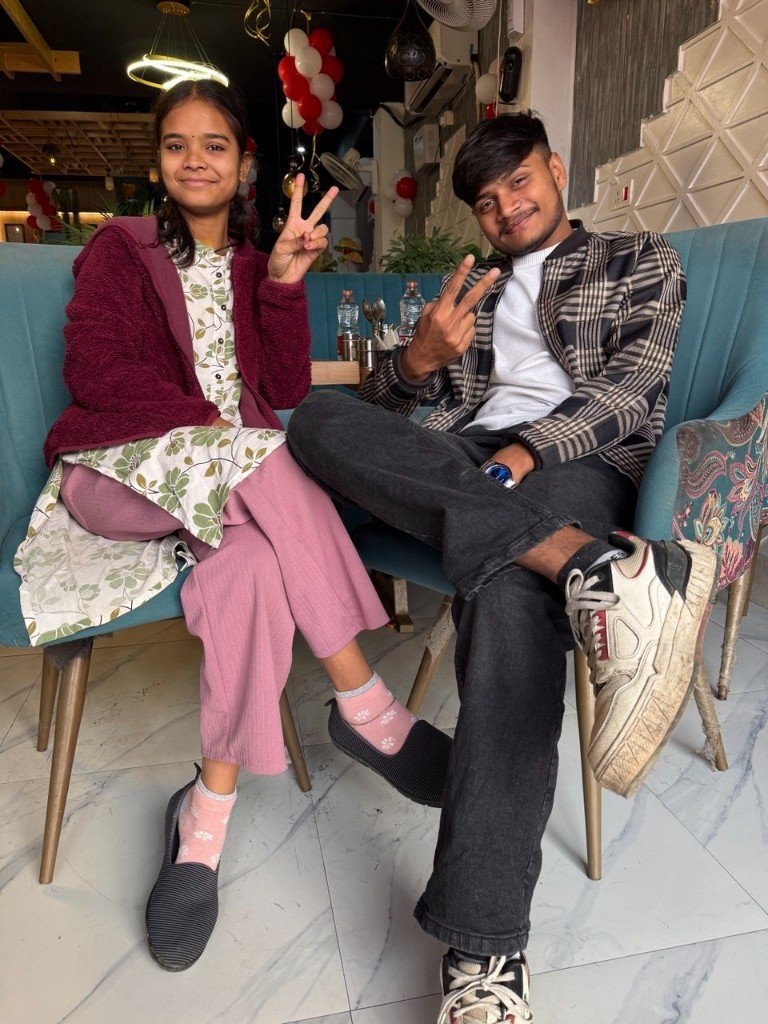 नीले सोफ़े पर गुड़िया और ओम, दोनों पीस का इशारा करते हुए